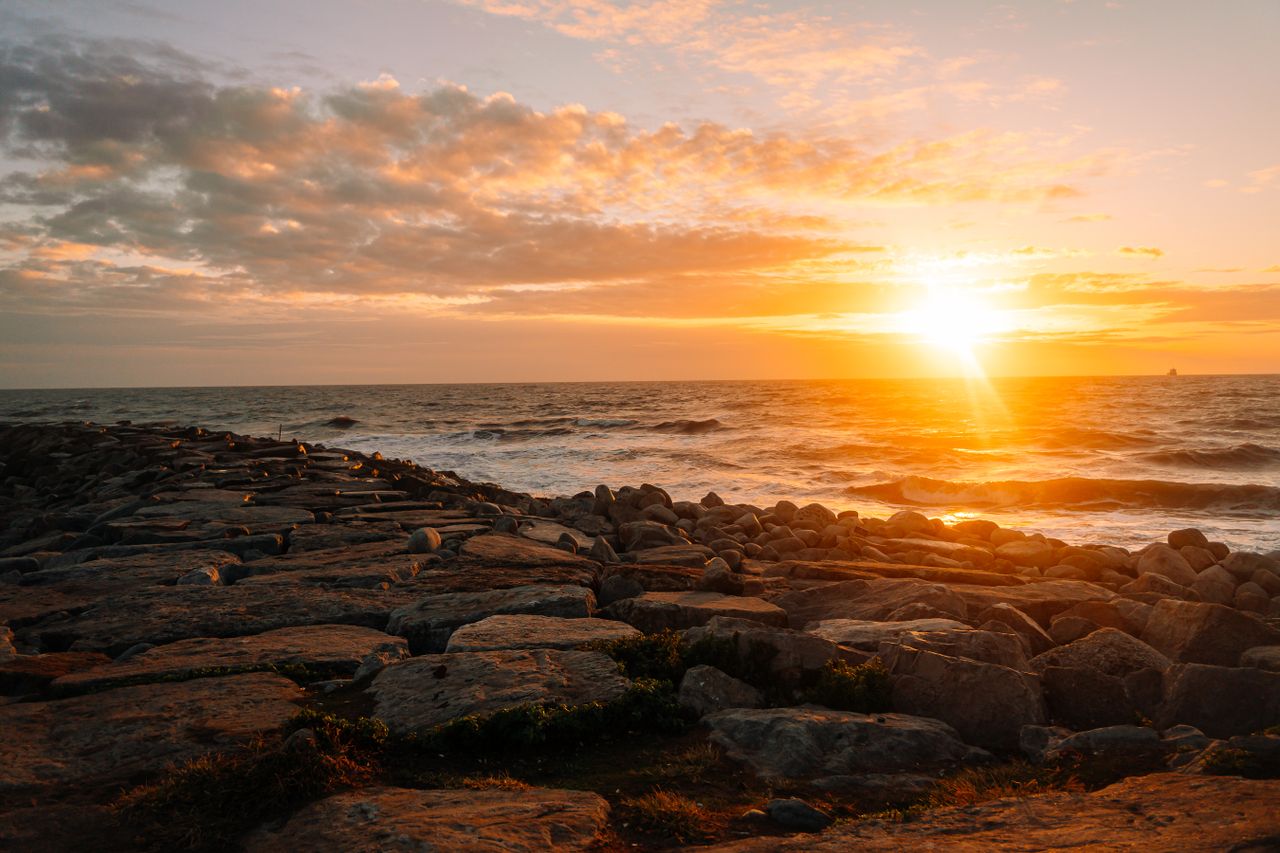 Home Stunning sunset view over rocky coastline, capturing vibrant hues of orange and gold in the sky.