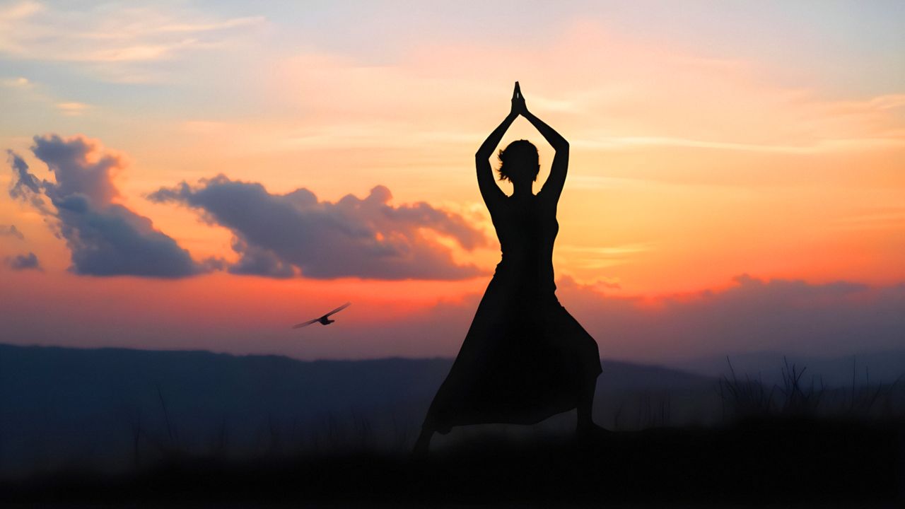 service-01 Silhouette of a woman practicing yoga during a serene sunset outdoors.